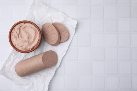 Delicious liver sausage and paste on white tiled table, flat lay. Space for text