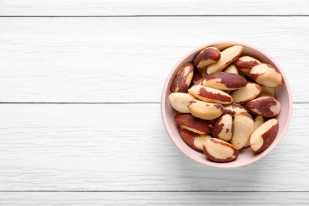 Bowl of delicious Brazil nuts on white wooden table, top view. Space for textの写真素材
