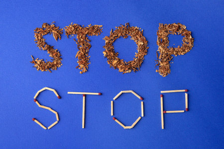 Words Stop made of dry tobacco and matches on blue background, flat lay. Quitting smoking conceptの写真素材