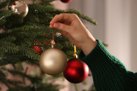 Woman decorating Christmas tree with beautiful golden bauble, closeupの写真素材