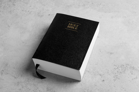 Bible with black cover on light gray table. Christian religious books