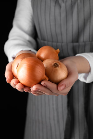 Woman holding ripe onions on black background, closeupの写真素材