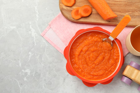 Healthy baby food. Bowl with delicious carrot puree on light gray marble table, flat lay. Space for textの写真素材
