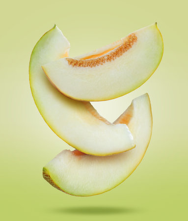 Delicious ripe melon slices falling on light green backgroundの写真素材