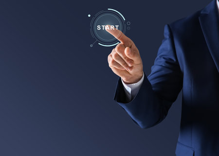 Man pressing start button on virtual screen against dark blue background, closeup. Space for textの写真素材