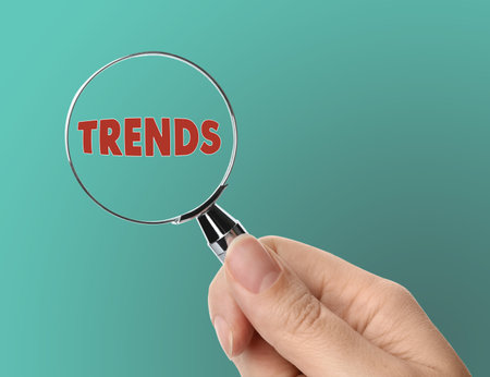 Searching new and popular trends. Woman holding magnifying glass over word on turquoise background, closeupの写真素材