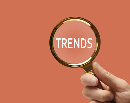 Searching new and popular trends. Woman holding magnifying glass over word on coral background, closeupの写真素材
