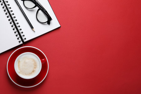 Cup with aromatic cappuccino, notepad, pencil and glasses on red background, flat lay. Space for textの写真素材
