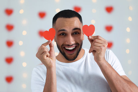 Handsome young man with red paper hearts indoors, view from camera. Valentine's day celebration in long distance relationshipの写真素材