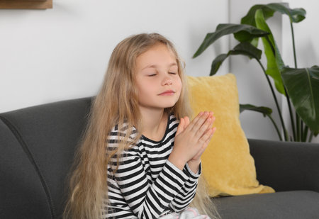 Girl with clasped hands praying on sofa at homeの写真素材