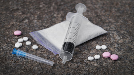 Plastic bag with powder, syringe and pills on stone surface, closeup. hard drugs