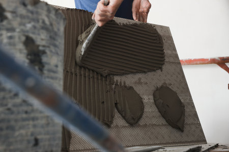 Worker applying cement on wall tile for installation indoors, closeup