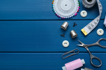 Flat lay composition with thimbles and different sewing tools on blue wooden table. Space for textの写真素材