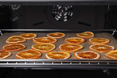 Many dry orange slices on parchment paper in ovenの写真素材