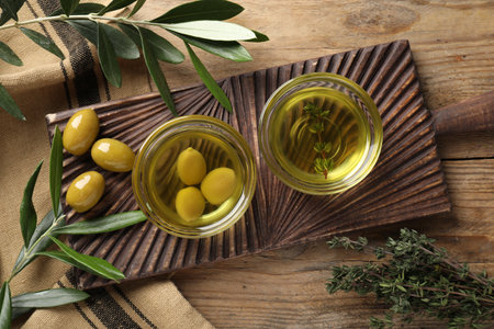 Flat lay composition with cooking oil and fresh olives on wooden table