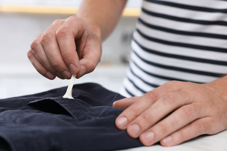 Man removing chewing gum from black jeans at white table indoors, closeupの写真素材