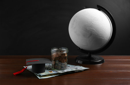 Scholarship concept. Graduation cap, money and globe on wooden tableの写真素材