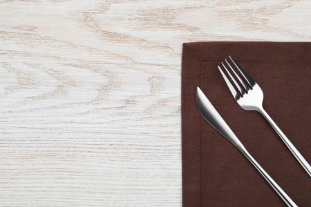 Fork, knife and napkin on white wooden table, top view with space for text. Stylish shiny cutlery...
