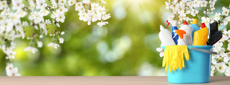 spring cleaning. Bucket with detergents and tools on wooden surface under blossoming tree against blurred green background, space for text. banner designの写真素材