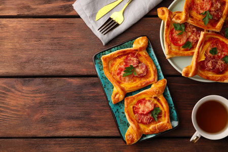 Fresh delicious puff pastry with cheese, tomatoes and parsley on wooden table, flat lay. Space for...