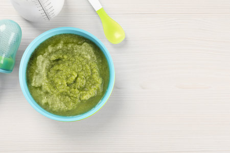 Healthy baby food. Bowl with tasty broccoli puree on white wooden table, flat lay and space for textの写真素材