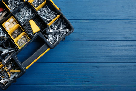 Plastic box with different furniture fittings and tools on blue wooden table, top view. Space for...
