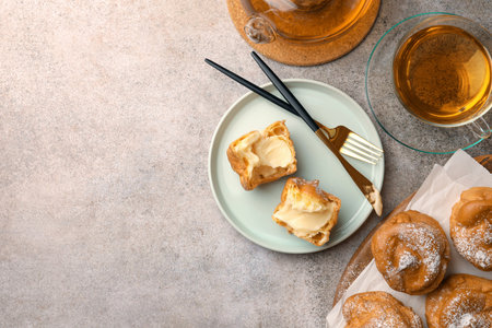 Delicious profiteroles filled with cream and tea on gray table, flat lay. Space for text