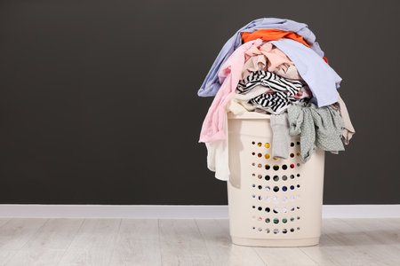 Laundry basket with clothes near dark gray wall. Space for textの写真素材
