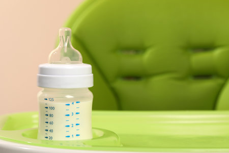 High chair with feeding bottle of infant formula on light green tray, closeup. Space for textの写真素材