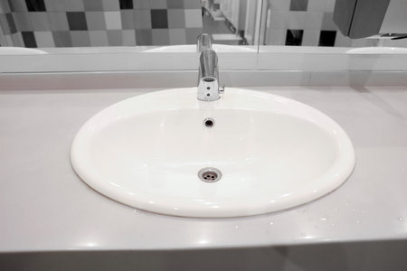 Clean ceramic sink near tiled wall in public toilet