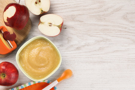 Healthy baby food. Bowl with delicious apple puree and fresh fruits on white wooden table, flat lay. Space for textの写真素材