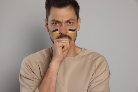 Angry man with drawings of Ukrainian flag on face against light gray backgroundの写真素材