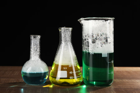 Laboratory glassware with colorful liquids on wooden table against black background. chemical reactionの写真素材
