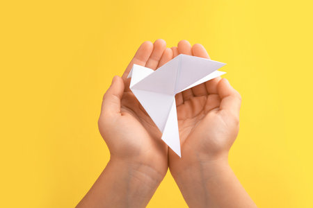 origami art. Child holding paper bird on yellow background, closeupの写真素材