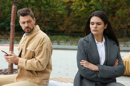 Upset arguing couple sitting on bench in park. Relationship problems