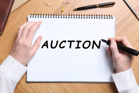 Woman writing word Auction in notebook at wooden table, top viewの写真素材