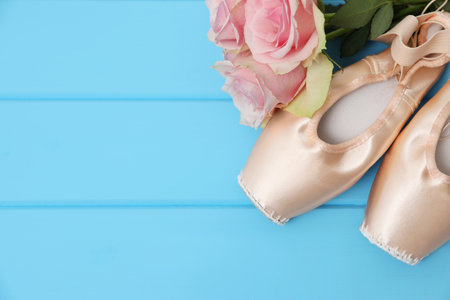 Beautiful beige ballet shoes and rose flowers on light blue wooden table, flat lay. Space for textの写真素材