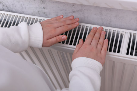 Girl warming hands on heating radiator indoors, closeupの写真素材