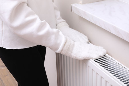 Girl warming hands on heating radiator indoors, closeupの写真素材