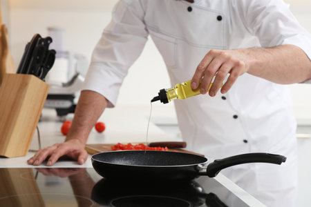 Chef pouring oil from bottle into frying pan indoors, closeupの写真素材