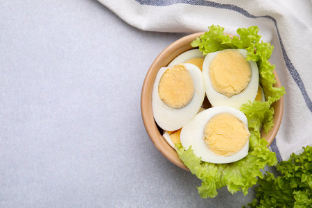 Fresh hard boiled eggs and lettuce on light gray table, top view. Space for textの写真素材