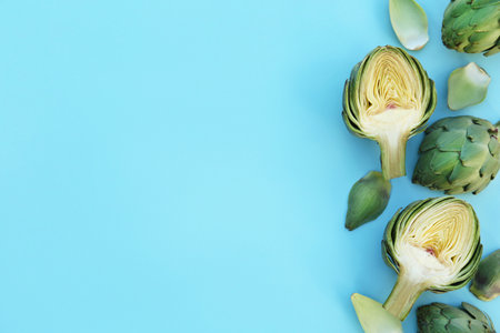 Whole and cut fresh raw artichokes on light blue background, flat lay. Space for textの写真素材