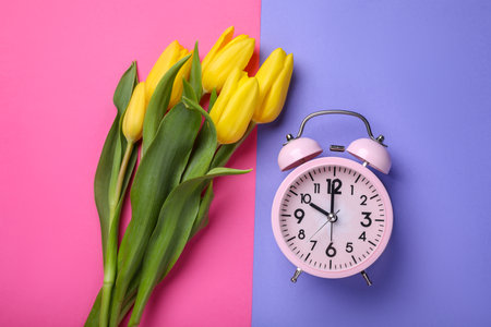 Pink alarm clock and beautiful tulips on color background, flat lay. spring timeの写真素材