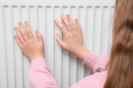 Girl warming hands on heating radiator, closeupの写真素材