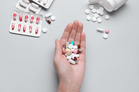 Woman holding colorful antidepressants on gray background, top view