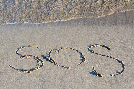 SOS message written on sand near seaの写真素材