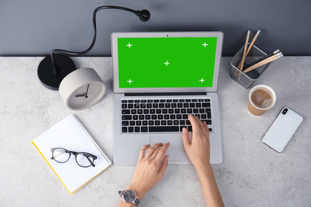 Young woman using laptop at desk, top view. Device display with chroma keyの写真素材