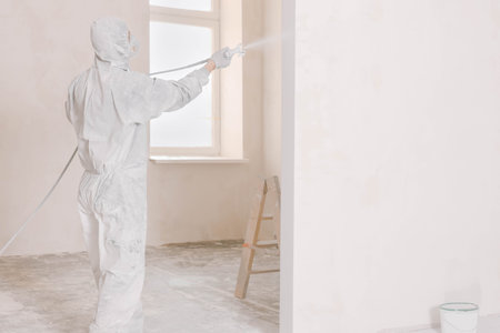 Decorator in uniform painting wall with sprayer indoorsの写真素材