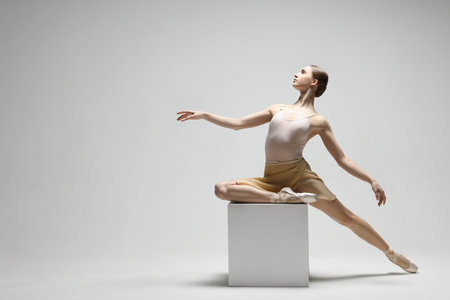Young ballerina practicing dance moves on cube against white background. Space for textの写真素材