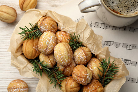 Homemade walnut shaped cookies with powdered sugar and fir branches in box on white wooden table,...